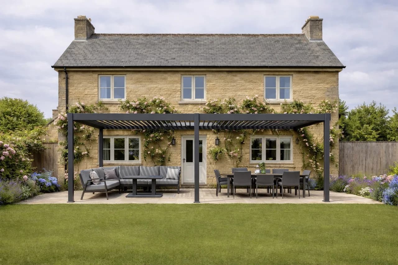 Large grey aluminium pergola with seating and dining areas outside a stone house