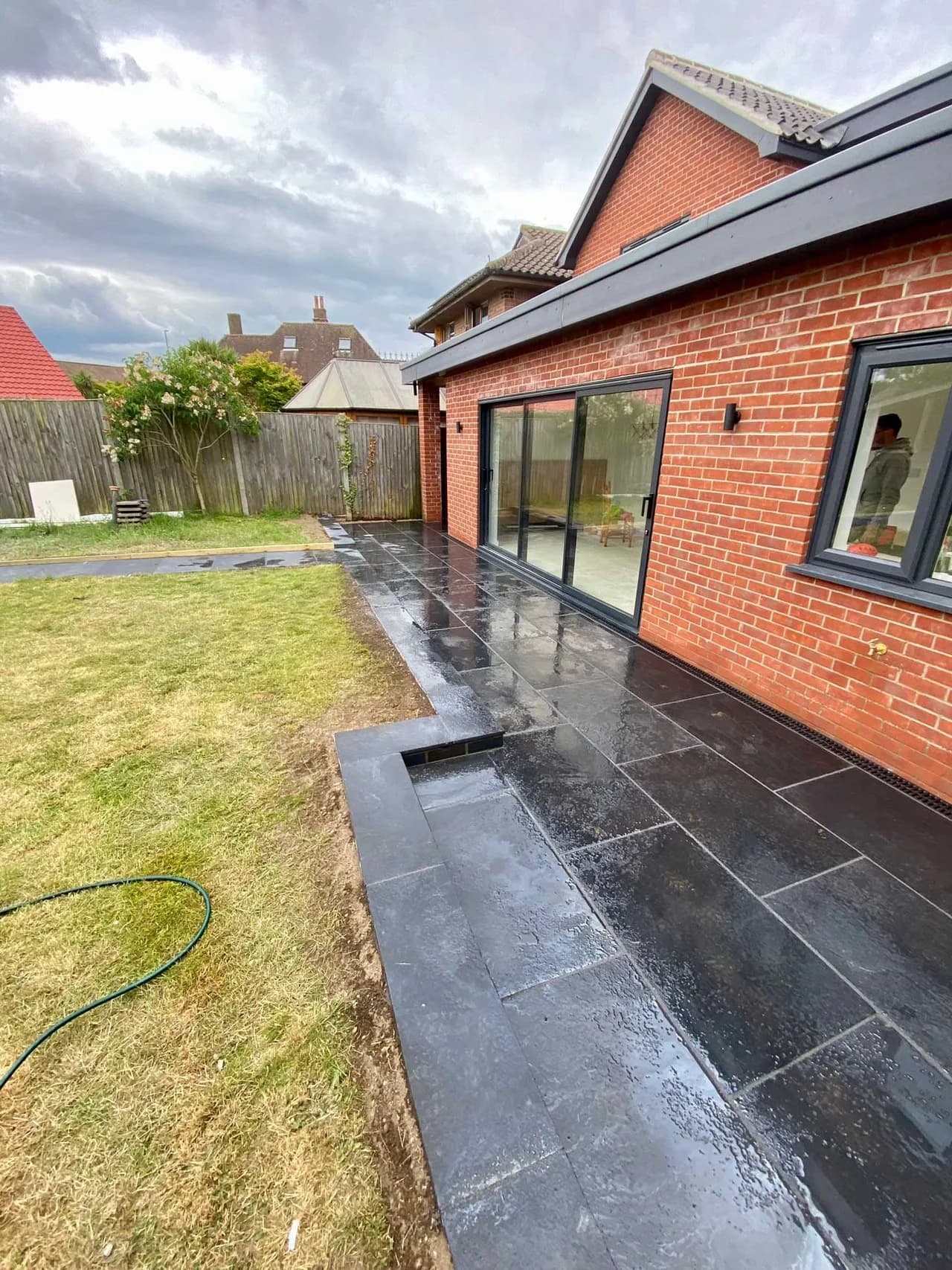 Dark paved patio wrapping around a brick house extension